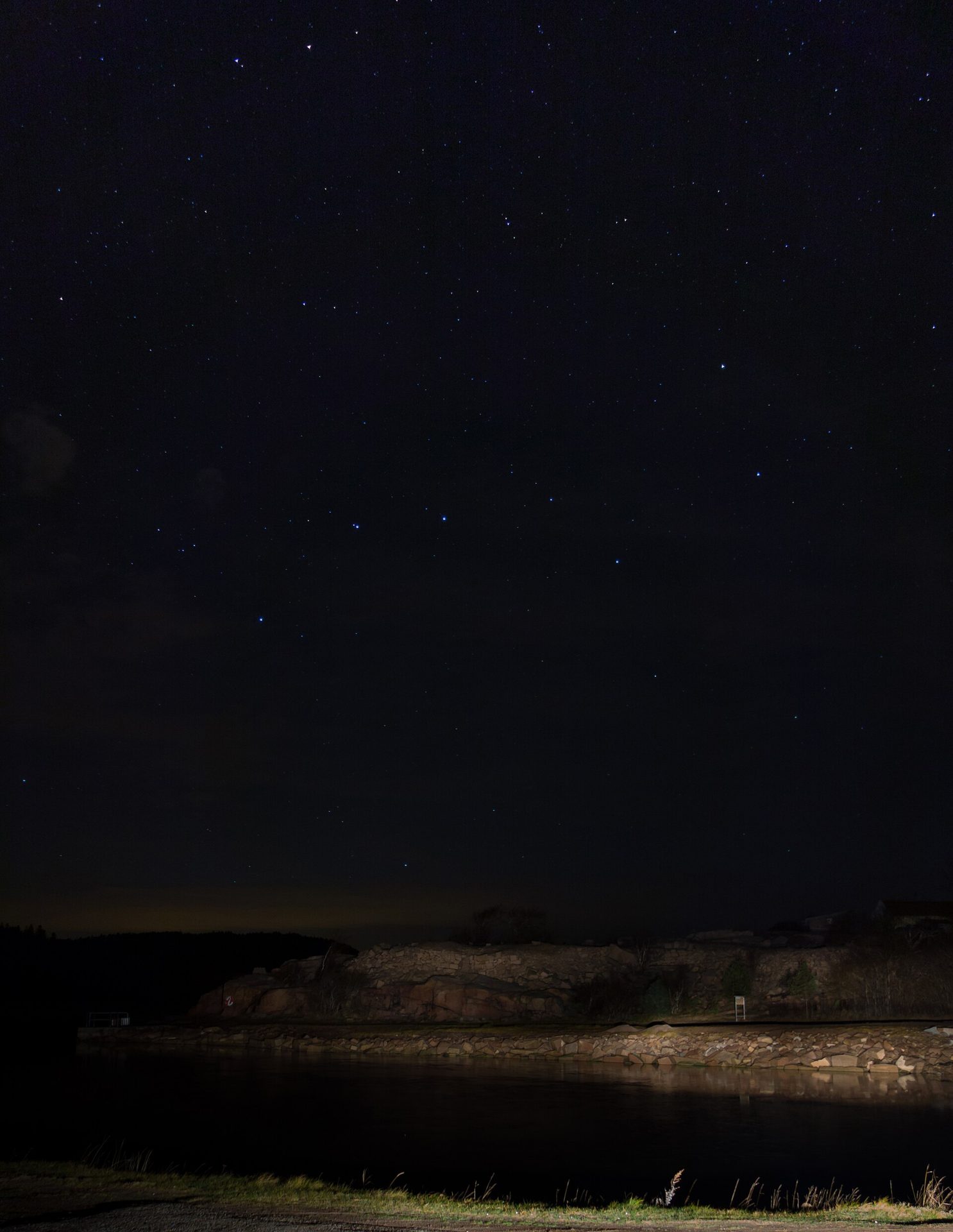 Headlights lighting a lakeshore under a starry night sky